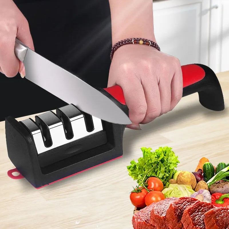 Kitchen 3/4-segment knife sharpener with black and red handle and stainless steel sharpening slots in use on a kitchen knife next to fresh vegetables and meat
